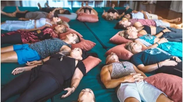 Group breathwork session: people lying on mats with pillows, eyes closed, mid-session