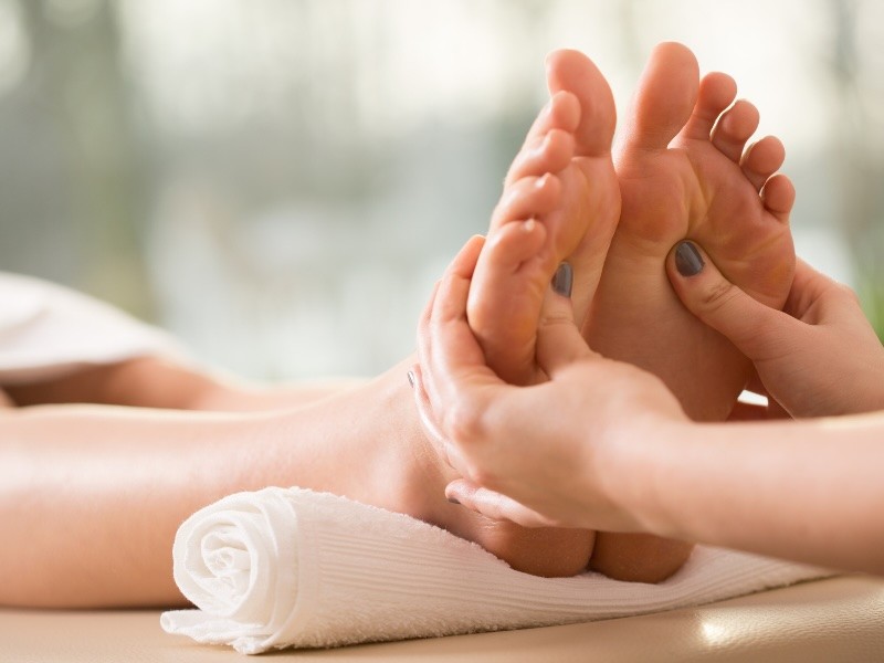 Foot reflexology session in progress: practitioner's hands working on client's feet, towel setup