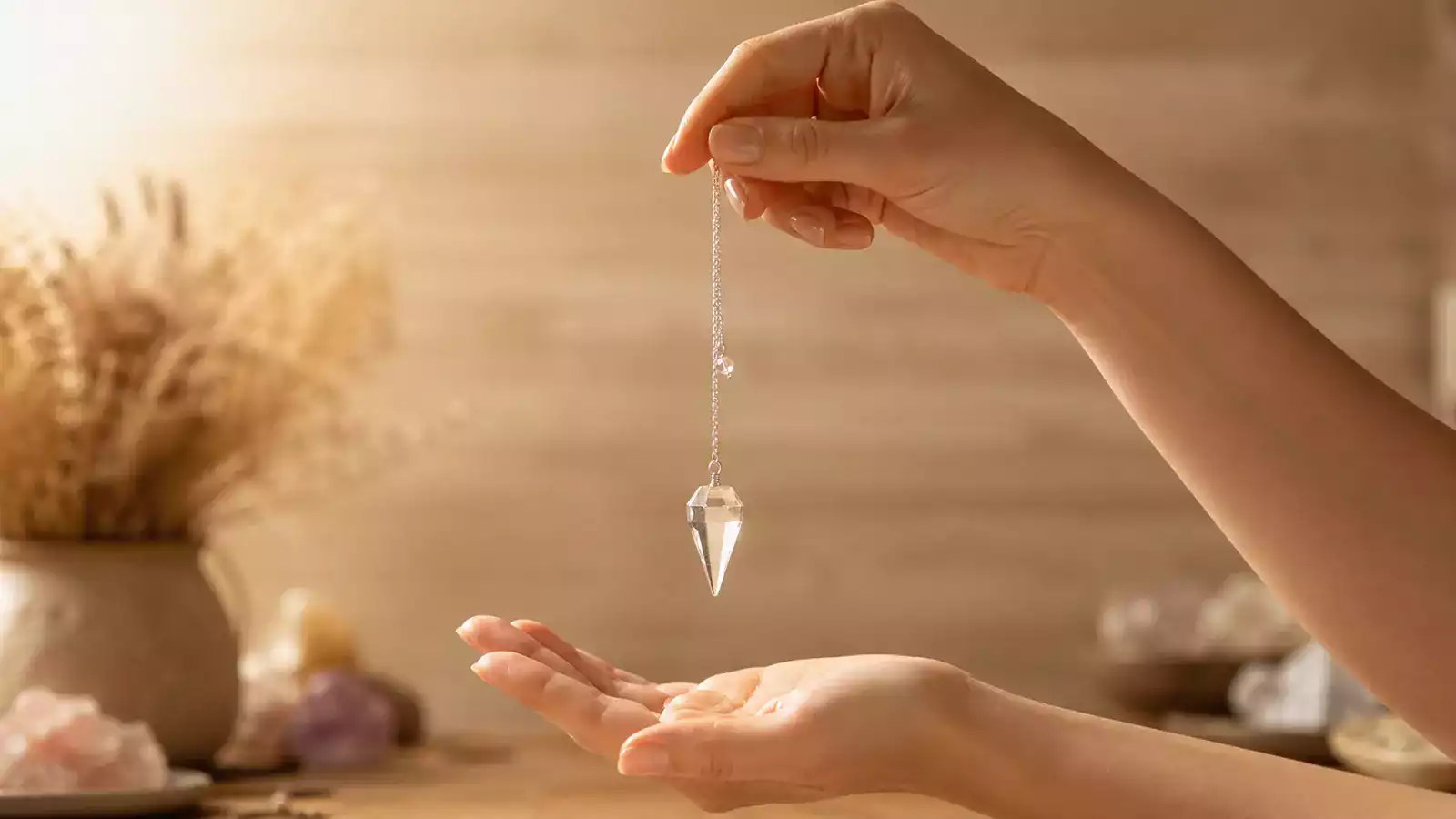 Hands holding faceted clear pendulum over open palm (visually verified real photo; dowsing blog)