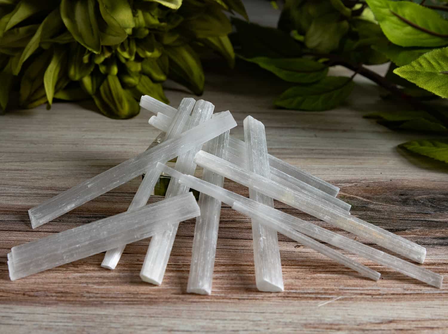 Slim selenite wands piled on wood, styled product shot