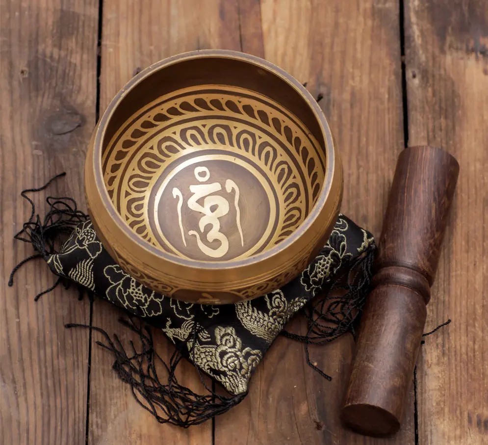 Mantra-etched bronze bowl with wooden mallet on silk